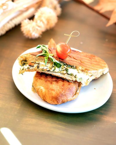 panini with chicken, spinach and feta on a white plate, on a restaurant table, a food photo, of high quality in the style of in the style of