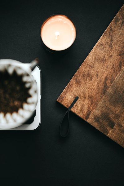 Top view of coffee filter on a black table with a wooden board and candle, in a minimalistic aesthetic style with a dark background and soft light, in the style of high resolution photography.