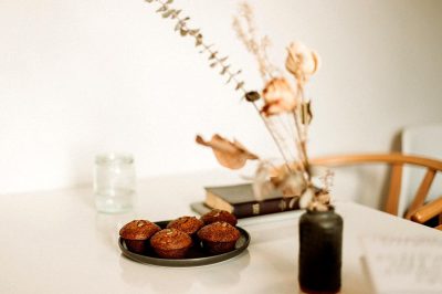 A plate of muffins on the table, a vase with dried flowers and books in the background, white walls, minimalism, captured in the style of Canon R5.