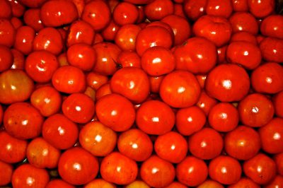 A pile of bright red tomatoes, highly detailed, in the middle of an indoor market, with a red background, taken from above. The photograph was taken using a Canon EFS f/5.6 lens and has a shallow depth of field. It was shot on Kodak Gold 400 film stock, in the style of street photography.