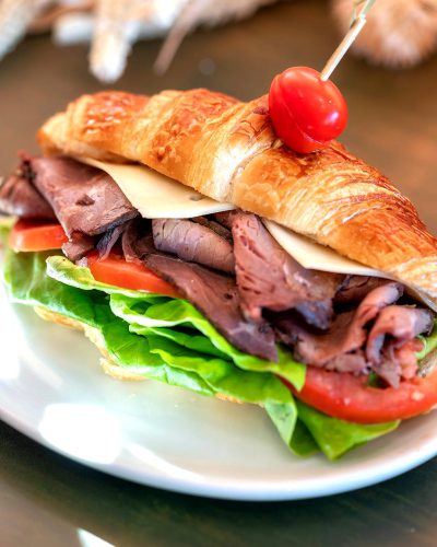roast beef sandwich with lettuce and tomato on a croissant, on a white plate, for food photography, in the style of instagram