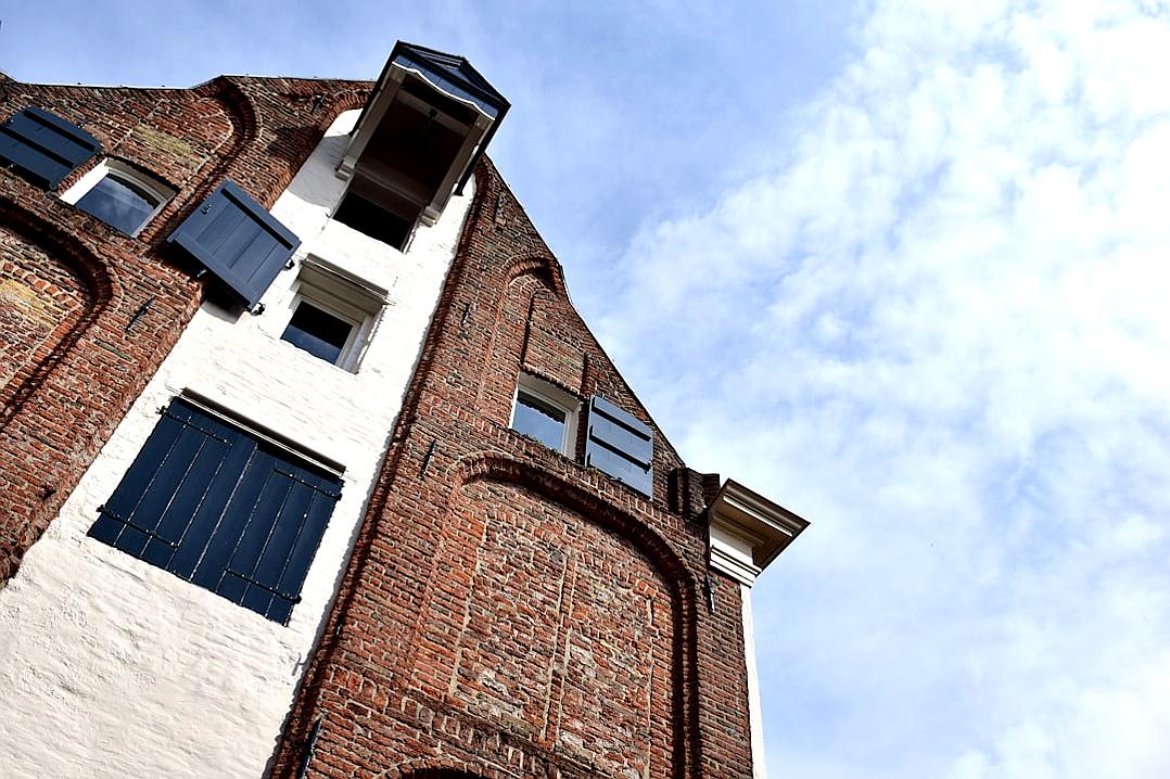 a wide angle photo of the side wall and roof, showing an old red brick building with white painted parts, black wooden shutters on windows, blue sky in background, camera looking up from ground level, architectural photography