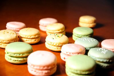 A photo of colorful macarons on a table, taken from above with soft lighting, shallow depth of field, and a closeup shot with a focus lens. The pastel colors include green, pink, yellow, white, and beige. They have delicate patterns with sprinkles of tiny beads or chocolate chips, creating an attractive visual appeal. This is suitable as a food magazine cover, showcasing delicious confectionery in its natural setting in the style of a magazine cover.