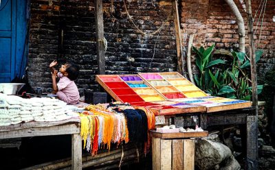 A colorful table with many different colored threads is set up on the street in an old village, and there's someone sitting next to it weaving silk scarves. The scene captures the essence of traditional Chinese textile production in its raw form. Shot by Nikon D850 camera with carmera lens at f/4 , high resolution photograph, natural lighting, ultra realistic photography